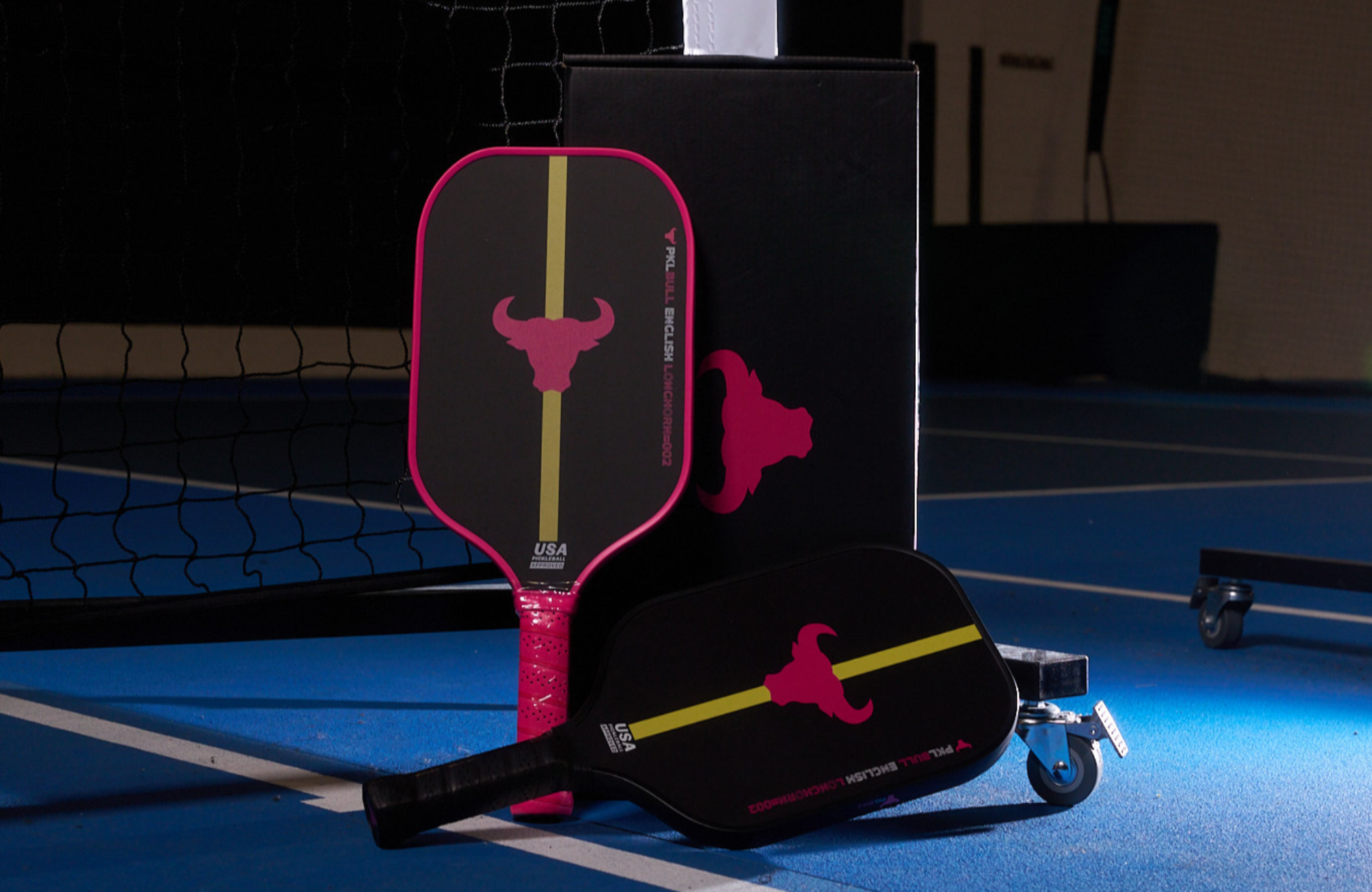 Pink and Black PKLBull Paddles positioned on indoor Pickleball court.